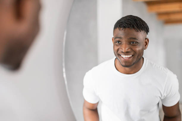 istock Black man smiling to his reflection in mirror in bathroom 2164336466