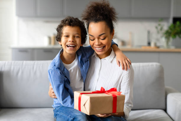 istock Joyful black mother and son with gift box on sofa 2164339091