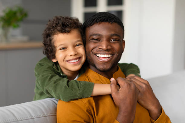 istock Cheerful black son hugs father from behind with bright smiles 2164339115