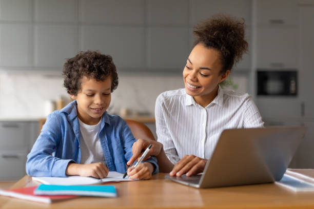 istock Black mother helps son with homework on laptop in well-lit kitchen 2164339149