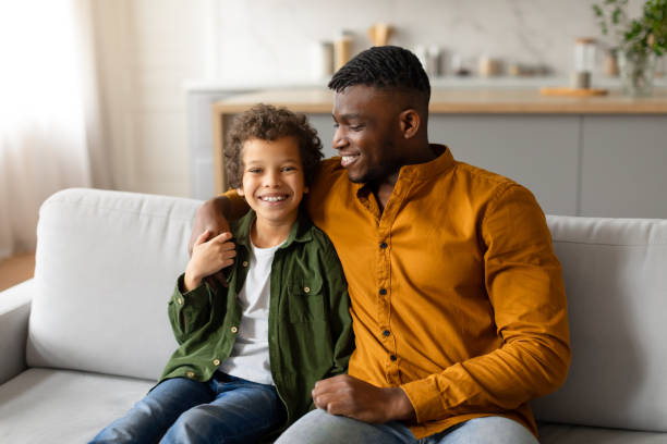 istock Happy black boy and dad sitting on couch at home 2164339180