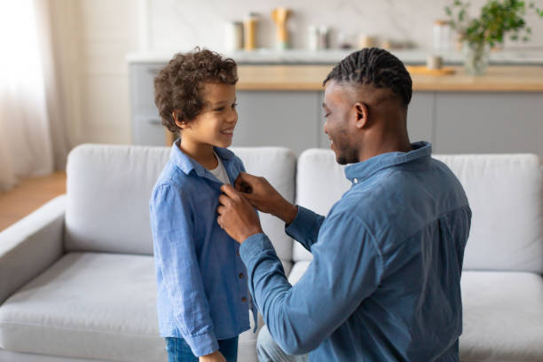 istock Young black father adjusting son's shirt, both smiling warmly 2164339190