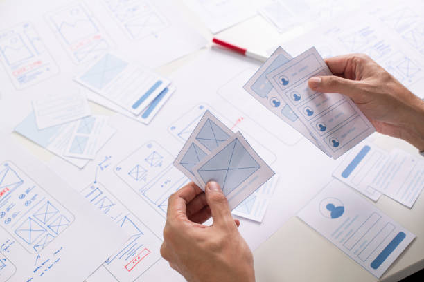 istock UX/UI designer working on wireframes for a website and mobile app prototype, surrounded by sketches of user-flow and design tools, in concept of website and mobile application design concept. 2164339332