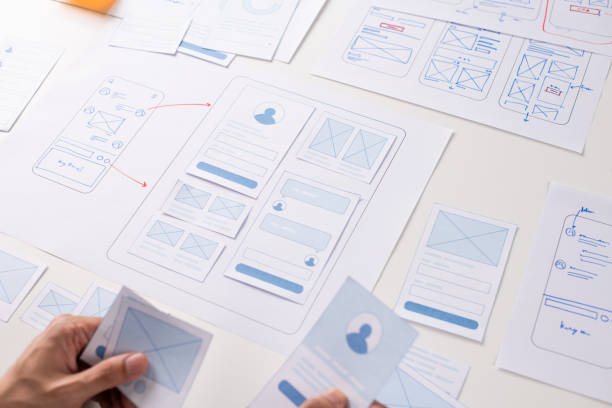 istock UX/UI designer working on wireframes for a website and mobile app prototype, surrounded by sketches of user-flow and design tools, in concept of website and mobile application design concept. 2164339334