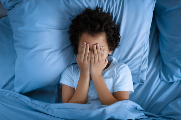 istock Young Boy Laying in Bed Covering Face With Hands 2164343145