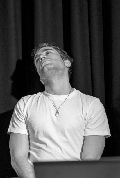 Rehearsals for a play.  A male actor around 25 looks contemplative on set in a white tee-shirt.