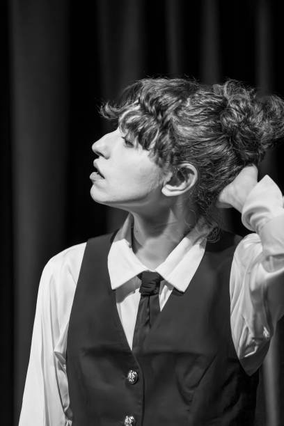 Rehearsals for a play. A female actress around 25 years old holds her head whilst listening to another actor.