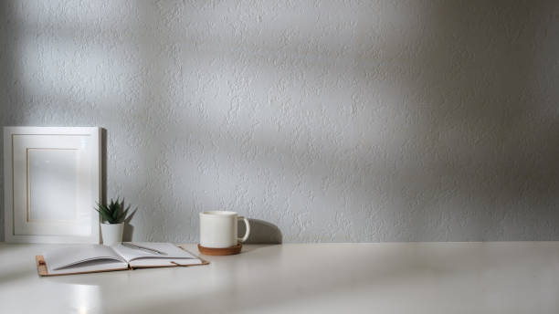 istock Comfortable workplace with picture frame, coffee, stationery and houseplant on white table. 2164374951