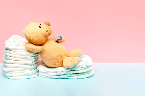 istock Stack of diapers with cute teddy bear,toy pacifier bottle lying on table. set for infant newborn boy girl for baby shower present gift on pink background copy space.Healthcare medical hygiene concept 2164376945
