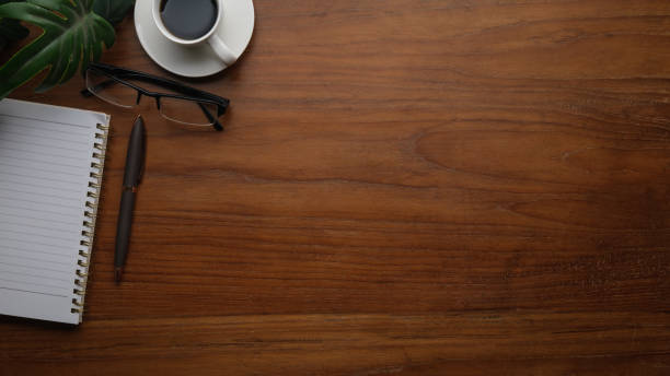 Top view of coffee cup, notebook and glasses on wooden table. Copy space for your text.