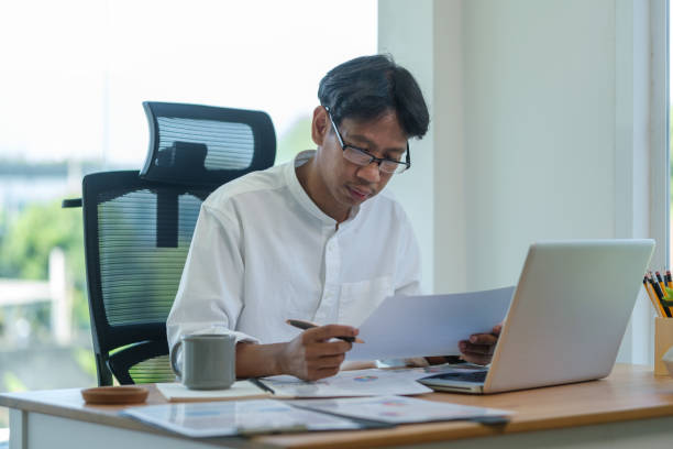 istock Focused businessman using laptop and reviewing documents at office. 2164379222