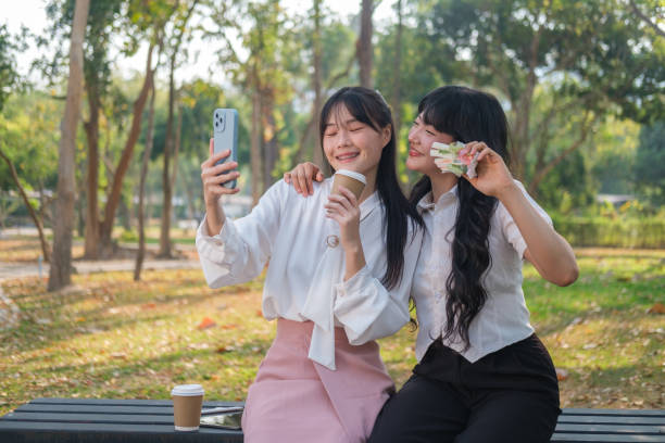 istock Two young women enjoy a lively moment outdoors, capturing a selfie together while holding coffee cups and a sandwich. 2164379761