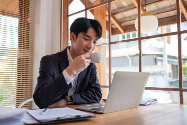 istock Businessman in a suit enjoys a coffee break while working on his laptop in a modern office. 2164379895