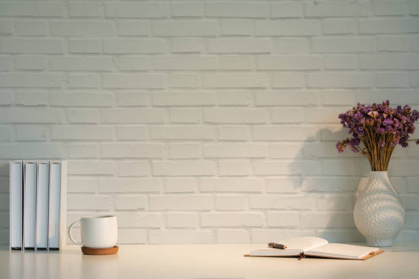 istock Workspace setup featuring a white brick wall background. On the left side of the desk, there are neatly organized white binders and a white mug on a coaster. 2164380879