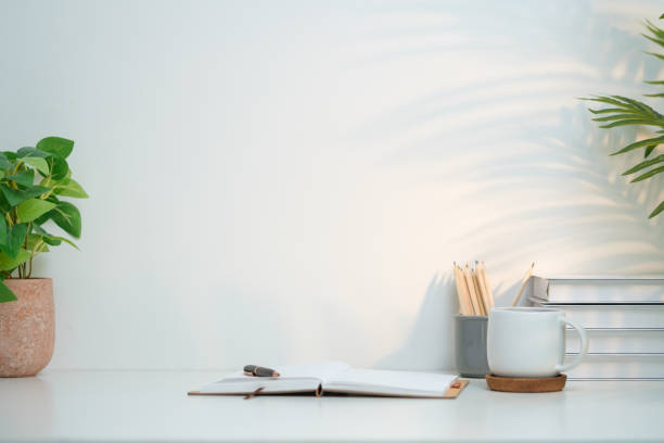 istock A clean and inviting minimalist workspace setup featuring a white desk against a pale wall. On the left side, a lush green potted plant adds a touch of nature and freshness to the space. 2164380890