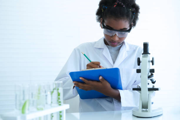 istock Black curly-haired child scientist holding clipboard to record experiment results at science laboratory. 2164385085