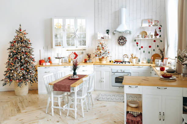istock White Scandinavian style kitchen decorated for Christmas. Dining table and Christmas tree with garland lights and red and silver Christmas toys. Christmas interior. Empty space 2164386642