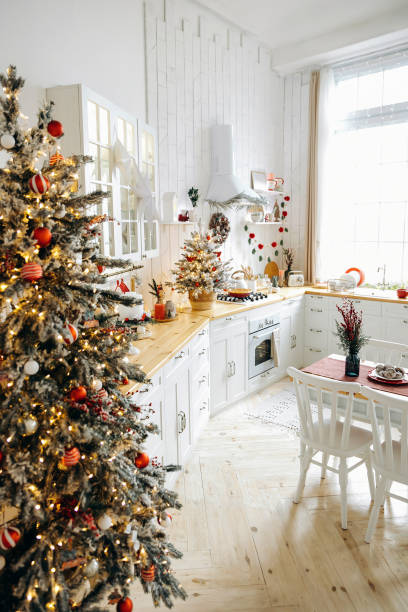 istock Christmas atmosphere on white Scandinavian kitchen with large windows, decorated with Christmas trees with garland lights and red toys. Empty space 2164386870