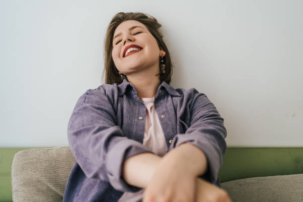 istock Cheerful plus-size woman sitting on couch, laughing with closed eyes. Relaxed, joyful expression, showcasing self-confidence and happiness. Body positivity and authentic emotions 2164392336