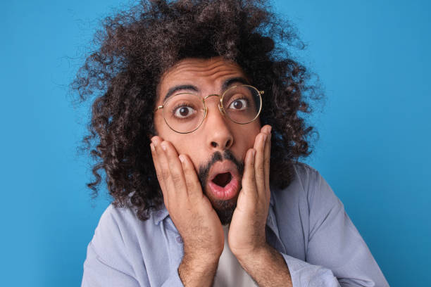 istock Surprised Man With Curly Hair Expressing Shock Against Blue Background 2164392807