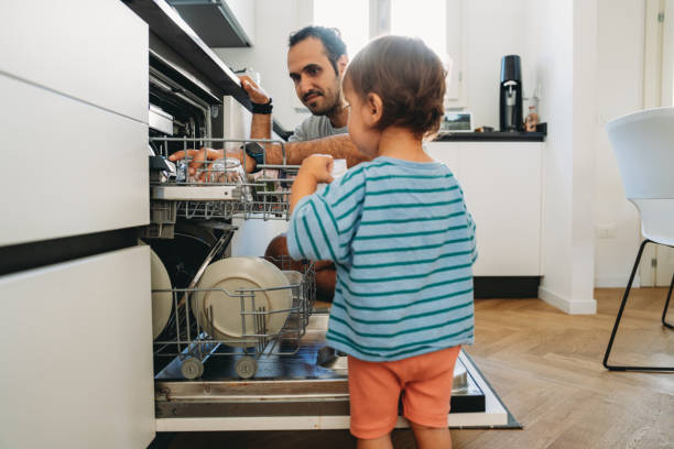 istock Father and son collaborating putting away dishes in dishwasher 2164393504