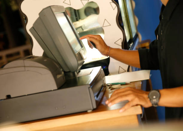 An unrecognizable woman near a laptop computer with a money counting machine sorts hundred dollar bills to exchange currency or deposit cash. The concept of finance, credit or exchange of volutes.