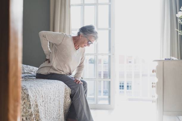 side view of senior woman resting on bed at home - dor de costas imagens e fotografias de stock