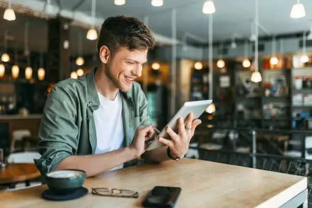 Young Man Reading and Using Digital Tablet in Bookstore Young Man Reading and Using Digital Tablet in Bookstore