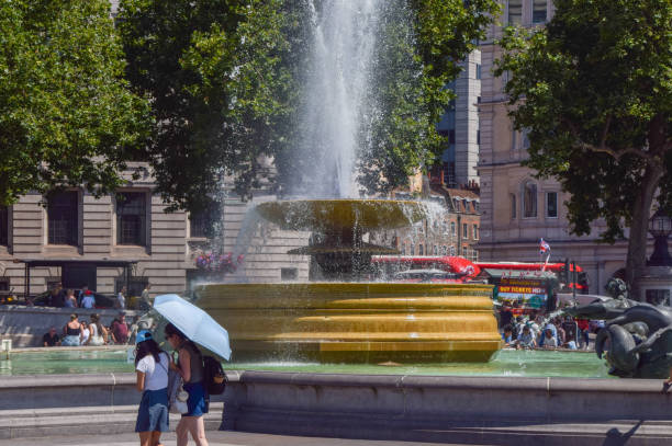 A lively crowd gathers around the iconic Trafalgar Square fountain on a sunny day, capturing the energy of central London.