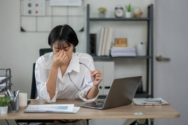 istock Exhausted female office worker feeling stressed, holding glasses, with laptop and documents on desk. 2164416833