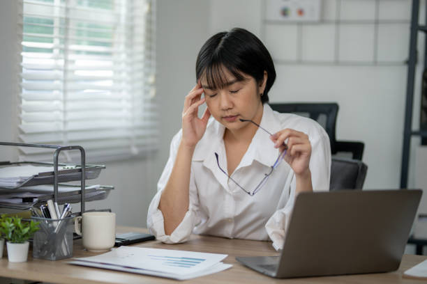 istock Exhausted female office worker feeling stressed, holding glasses, with laptop and documents on desk. 2164417126