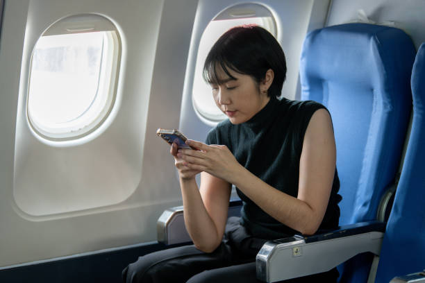 A concentrated woman uses her smartphone while seated by the airplane window, possibly managing work or personal matters.