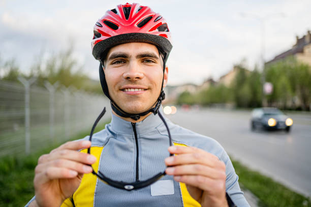 Young smiling cyclist putting on sunglasses