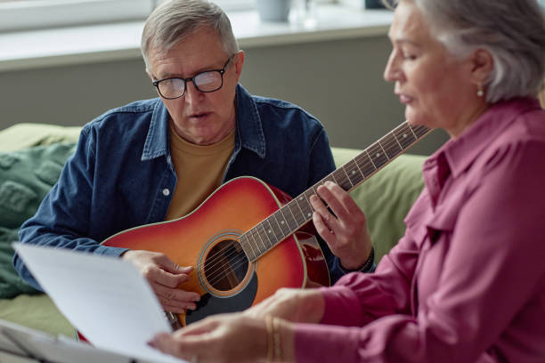 istock Mature Man Playing Guitar Reading Lyrics Singing 2164427144