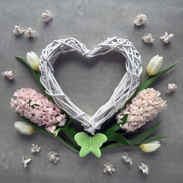 A heart-shaped wreath with spring flowers, tulips and hyacinth, with a colorful ceramic butterfly.
