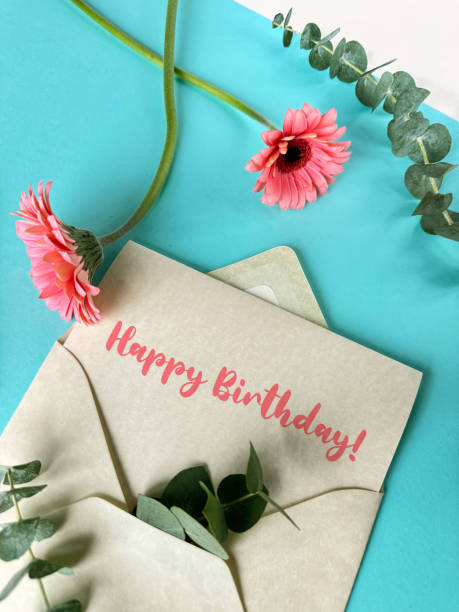 A pink envelope with a green birthday card placed inside, with pink gerbera flowers on white table