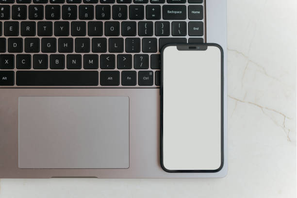 istock Mobile phone with blank screen lying on laptop keyboard. Top view, flat lay 2164458421