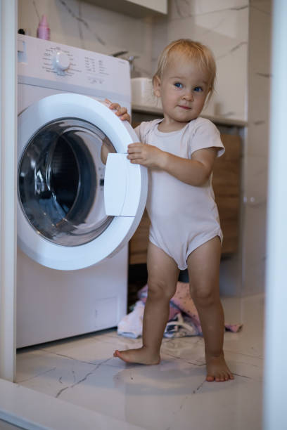 istock Two year old child doing household chores. Loading washing machine. 2164459852