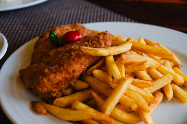 A plate of breaded fish fillets served with a generous portion of golden French fries. The dish is garnished with a small tomato slice and parsley, offering a classic and satisfying meal.