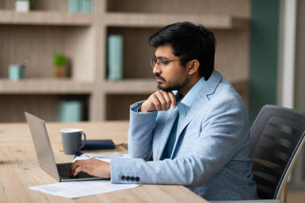 istock Indian manager looks at laptop deep in thought in office 2164474014