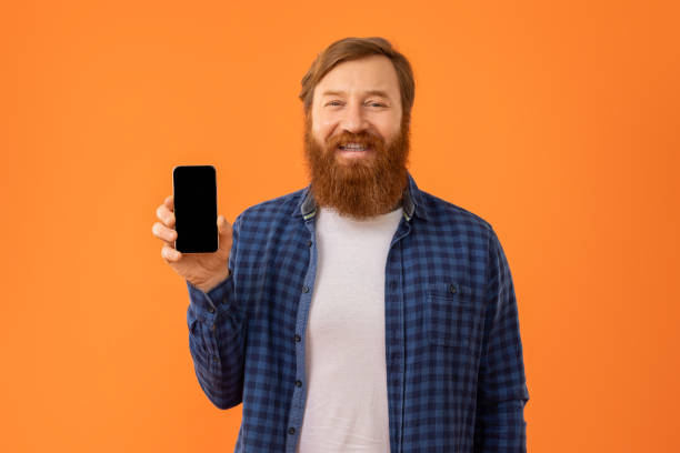 istock Positive redhaired bearded man showing his smartphone blank screen, studio 2164475868