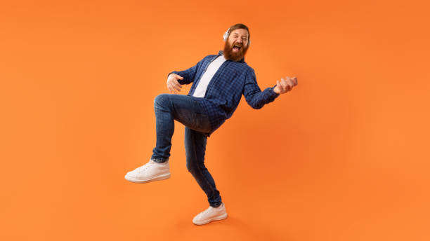 istock Energetic guy enjoying music through headphones playing invisible guitar, studio 2164475874