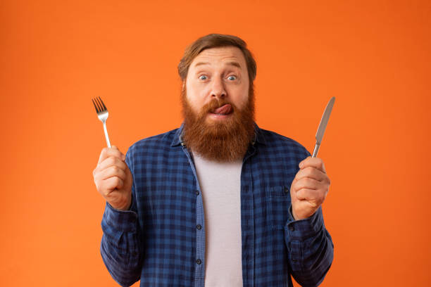 istock Hungry redhaired bearded guy holding knife and fork, orange background 2164475888