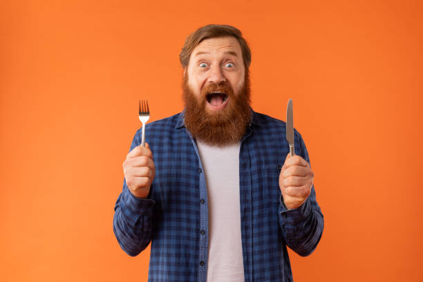 istock Hungry bearded man holds knife and fork expressing excitement, studio 2164475890