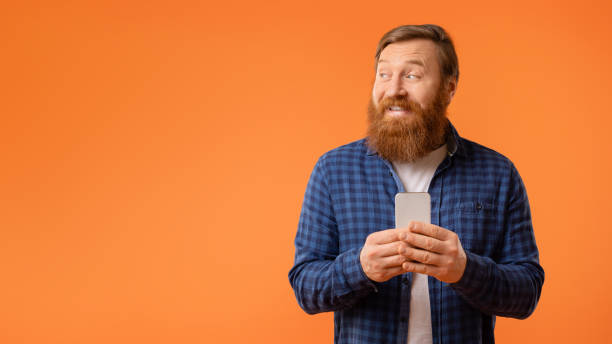 istock bearded man holding phone looking aside at blank space, studio 2164475903