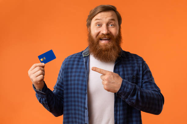 istock Excited Redhaired Bearded Guy Showing Credit Card Over Orange Background 2164476041