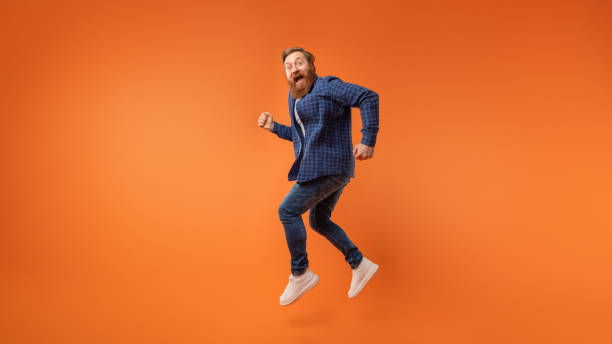 istock Excited redhaired bearded guy jumping and shouting over orange backdrop 2164476047