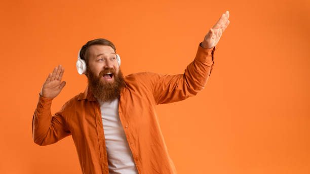 istock Positive Bearded Guy In Wireless Headset Dancing Over Orange Wall 2164476074