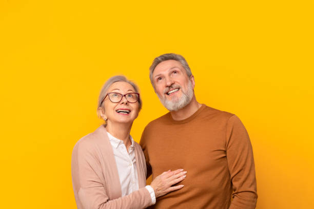 istock Cheerful senior couple posing together hugging looking up, yellow background 2164478043