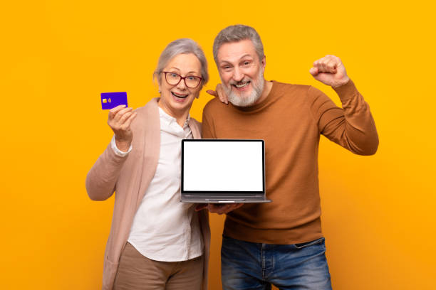 istock senior couple holding bank card showing laptop empty screen, studio 2164478048